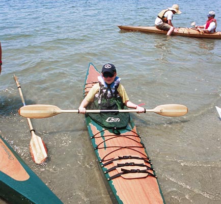 A young paddler coming ashore with a Chesapeake 14 wooden kayak