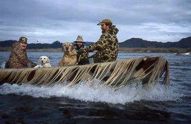 Camouflage hides the hull of the Cackler as three men and their dogs apparently float on a pile of grass.