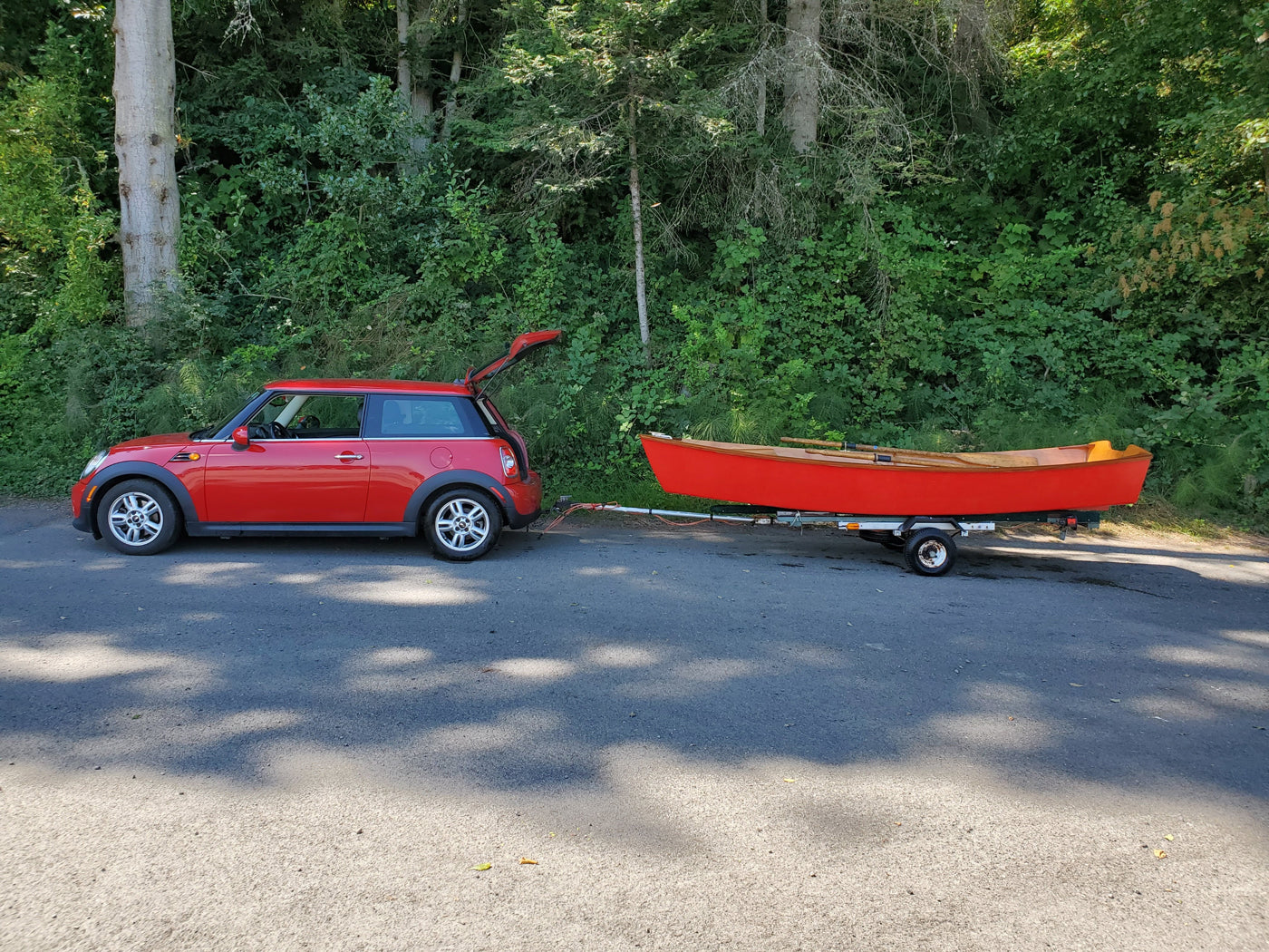 Red Jimmy Skiff hull on a trailer behind a red Mini. 