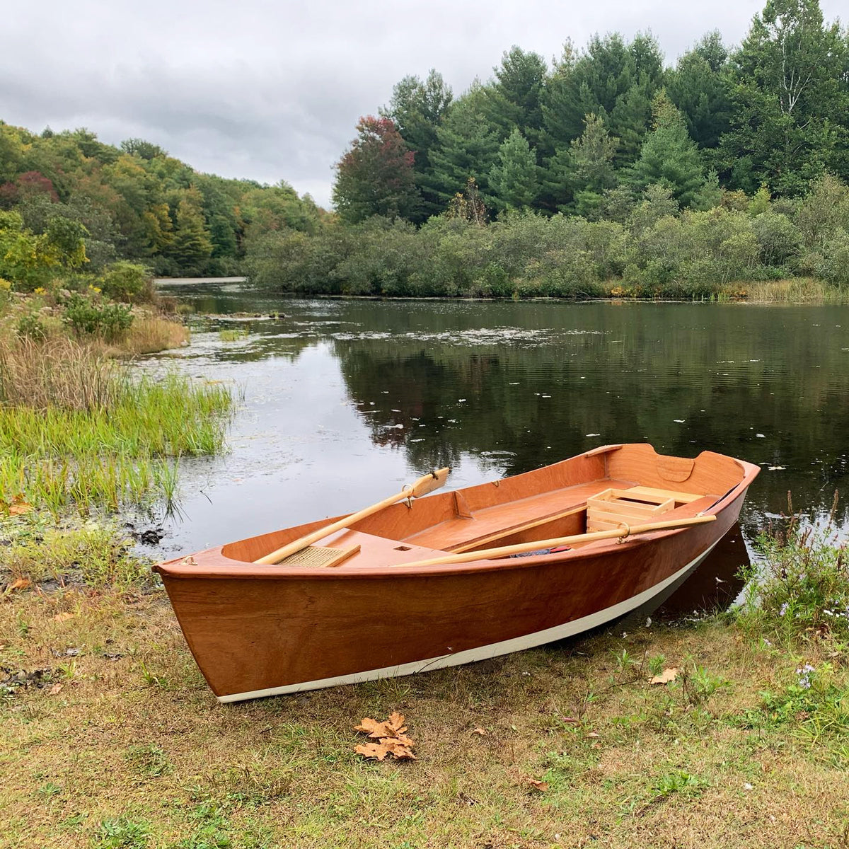 Customer built Jimmy Skiff on a lake shoreline. Varnished interior and exterior, with a white bottom.