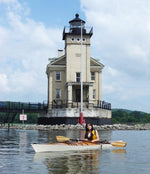 A woman paddling a Chesapeake 16LT wooden kayak in front of a lighthouse Thumbnail